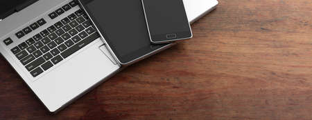 Mobile phone and tablet with blank black screens and a computer laptop on wooden background, copy space. 3d illustrationの写真素材