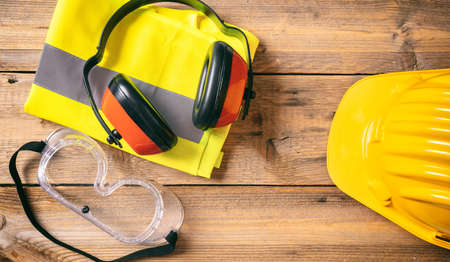 Construction site safety. Protective hard hat, headphones and glasses on wooden background, copy space, top viewの写真素材