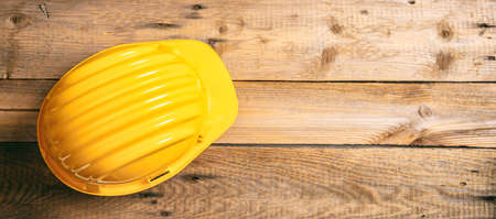 Construction site safety. Yellow protective hard hat on wooden background, copy space, top viewの写真素材