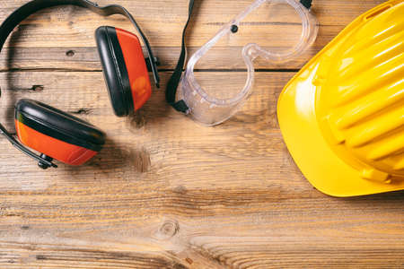 Construction site safety. Protective hard hat, headphones and glasses on wooden background, copy...