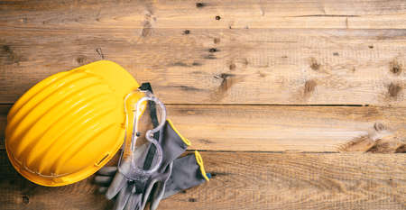Construction site safety. Protective hard hat, gloves and glasses on wooden background, copy space, top viewの写真素材