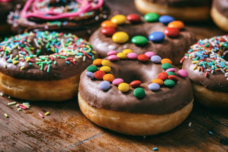 Pastries concept. Donuts with chocolate glaze and sprinkles, on wooden table blurry background.の写真素材