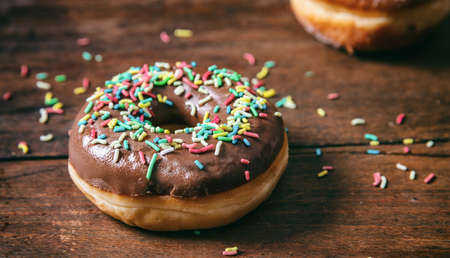 Pastries concept. Donut with chocolate glaze with sprinkles, isolated on wooden table blurry...