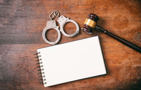 Law and order concept. Handcuffs, gavel and a notebook on a wooden background with copy space.の写真素材