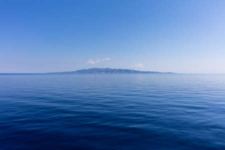 Greece. Aegean sea, Cyclades. Small cycladic island on blue sky and calm sea water backgroundの写真素材