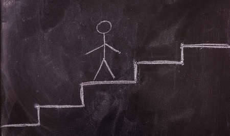 Success concept. Stick man going up the ladder drawing, isolated, on a blackboard.