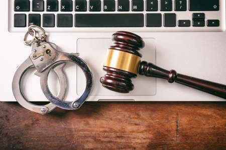 Cybercrime and law concept. Handcuffs and a judge gavel on a computer on a wooden background, copy...