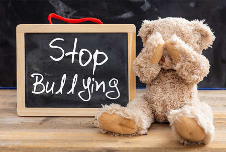 Bullying at school. Teddy bear covering eyes and stop bullying text on a blackboard