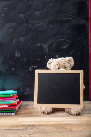 Back to school. Teddy bear and blank blackboard with frame on wooden desk, space for textの写真素材