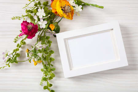 Flower bouquet and a blank white photo frame, top view, copy space, on a white wooden background.