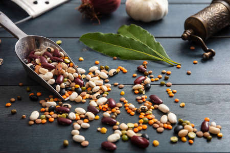 Healthy diet concept. Close up of assortment of legumes in a stainless scoop, spilled on a wooden tabletop background, pepper grinder, onion, garlic and grater.の写真素材