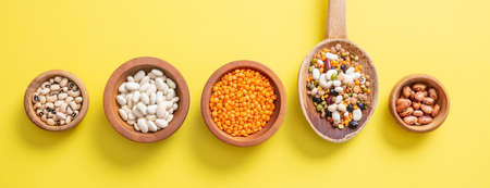 Healthy diet concept. Assortment of legumes in wooden bowls on yellow background, isolated, top view, banner.の写真素材