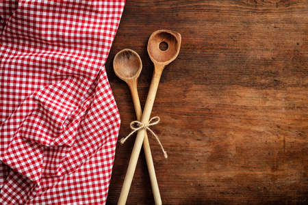 Wooden kitchen utensils and red and white checkered picnic tablecloth on wooden table, top view, copy spaceの写真素材