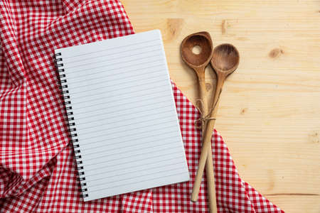 Cooking recipe.Blank notebook, kitchen utensils and red tablecloth on wooden table, top view, copy spaceの写真素材