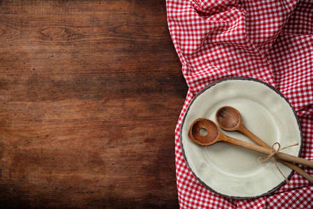 Rustic place setting. Empty plate, kitchen utensils and red tablecloth on wooden table, top view, copy spaceの写真素材