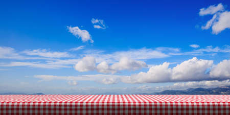 Table covered with red checkered tablecloth on blue sky background, copy space. 3d illustrationの写真素材