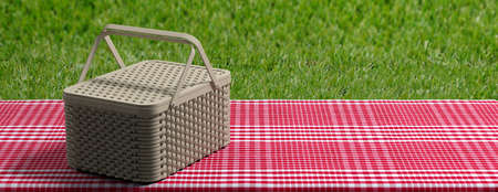 Picnic wicker basket on red checkered tablecloth, green grass background, banner, copy space. 3d illustrationの写真素材
