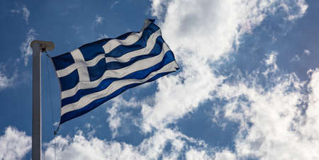 Greek flag on flagpole waving on blue cloudy sky backgroundの写真素材