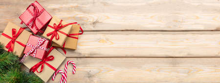 Christmas time. Gift boxes with red ribbons and candy canes on wooden background, banner, copy...