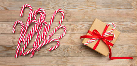 Christmas time. Candy canes and a gift box with red ribbon on wooden background, top viewの写真素材