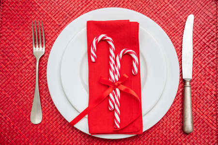 Christmas table setting. Candy canes on white plates and cutlery, red mat, top viewの写真素材
