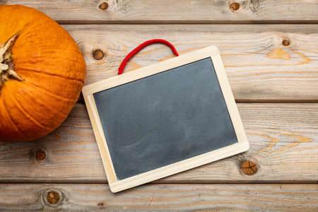 Halloween, thanksgiving. Pumpkin and blank blackboard on wooden backgroound, copy space, top viewの写真素材