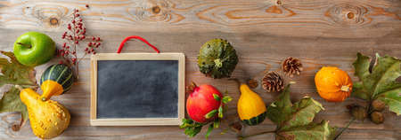 Thanksgiving concept. Colorful pumpkins, fruits and blank blackboard on rustic wooden background, copy space, bannerの写真素材