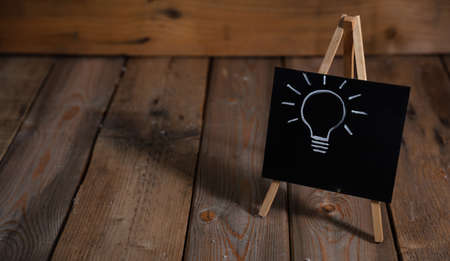 Idea concept. Light bulb drawn on a chalkboard, dark wooden background, copy spaceの写真素材