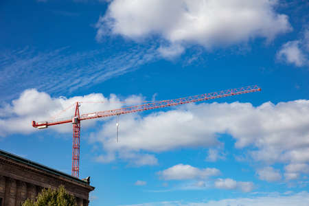 Under construction. Red tower crane on blue sky background