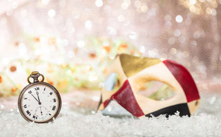 Carnival party countdown. Minutes to midnight on an old watch, colorful mask, bokeh festive backgroundの写真素材