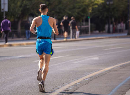 Running in the city roads. Young man runner, back view, blur background, copy spaceの写真素材