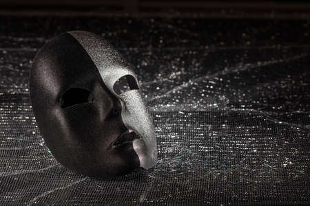 Two faced carnival mask, half black, half silver on black shiny background, closeup view, copy spaceの写真素材