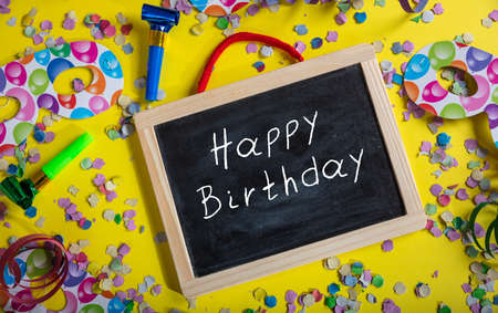 Birthday party. Happy birthday text on a blackboard, confetti and serpentines on bright yellow...