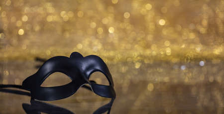 Carnival time. Venetian black mask on golden bokeh background, reflections, copy spaceの写真素材