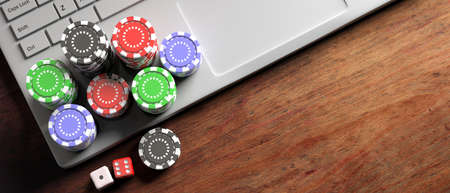 Online casino, betting concept. Poker chips and dice on computer laptop, wooden background, banner, top view, copy space. 3d illustrationの写真素材