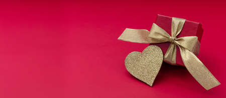 Valentines day love gift box. Red gift and shiny gold heart on red background, banner, view from above, copy spaceの写真素材