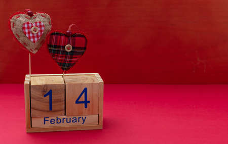 Valentines day.  Calendar wooden cubes with 14 February text and two red fabric hearts, against red background, copy spaceの写真素材