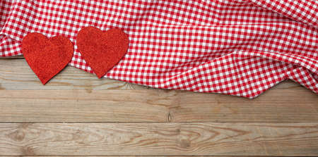 Valentines day. Top view of red fabric hearts and checkered white and red cloth against wooden backgroundの写真素材