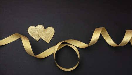 Valentines day.  Top view of two golden hearts with satin ribbon against black background, wallpaper.の写真素材