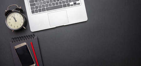 Time management concept. Computer laptop and alarm clock on black color office desk, banner, top...