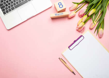 Womens day concept. Pink tulips bouquet, date March 8th and computer laptop on pink pastel...