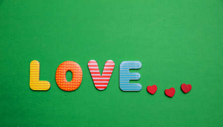 Love text with colorful letters and small red hearts on green color backgroundの写真素材