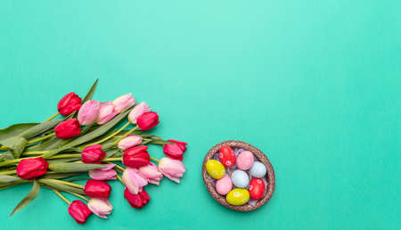 Easter eggs, pastel colors painted and tulips bouquet, green background, top view, copy space