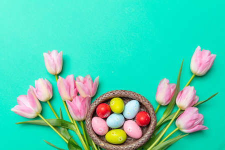 Easter eggs, pastel colors painted and pink tulips bouquet, green background, top view, copy space