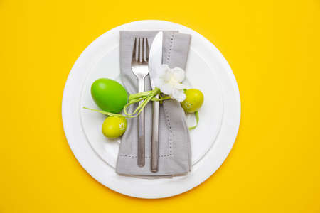 Easter table, place setting. Easter eggs, green color painted in a white plate, yellow background,...