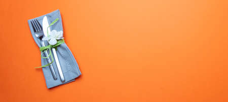 Table place setting in orange color. Gray linen napkin with decoration and cutlery on orange color background, banner, top view,の写真素材