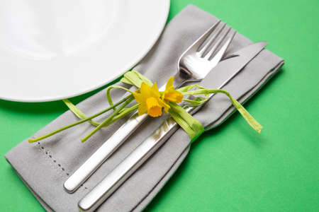 Table place setting in bright green. Gray linen napkin with decoration and white plate on green...