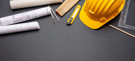 Architect engineer workplace, construction site desk. Project blueprints, yellow hard hat and engineering tools on black, banner, copy spaceの写真素材