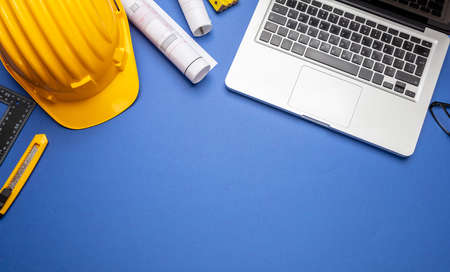 Architect engineer construction site office desk. Project blueprints, yellow hard hat and computer...