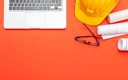 Architect engineer construction site office desk. Project blueprints, yellow hard hat and computer laptop on orange color, top view, copy spaceの写真素材